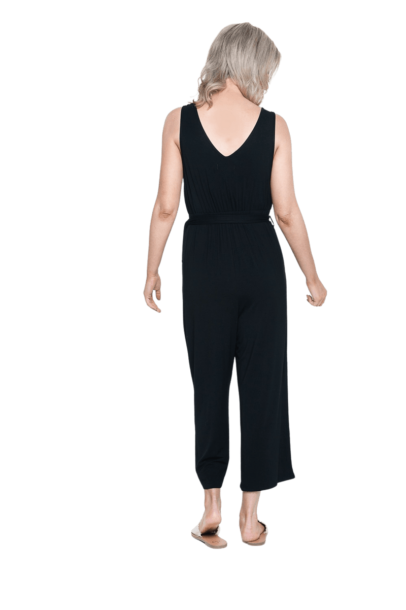 Petite model facing the back wearing black sleeveless, ankle-length jumpsuit, featuring crossover neckline, waist belt and pockets. Jesse available in sizes 6-26