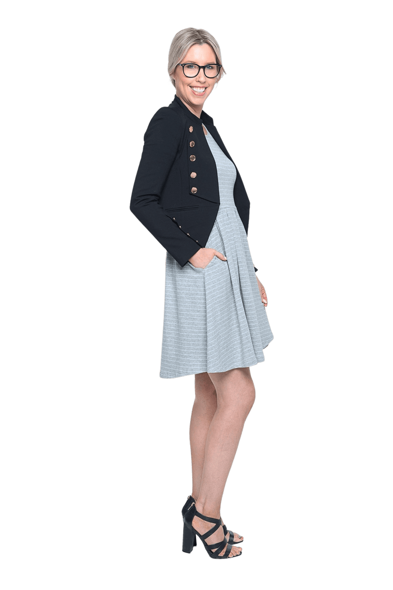 Petite model facing the side wearing grey with white pin striped, knee length dress paired with a black blazer and glasses. Kaitlyn available in sizes 6-26