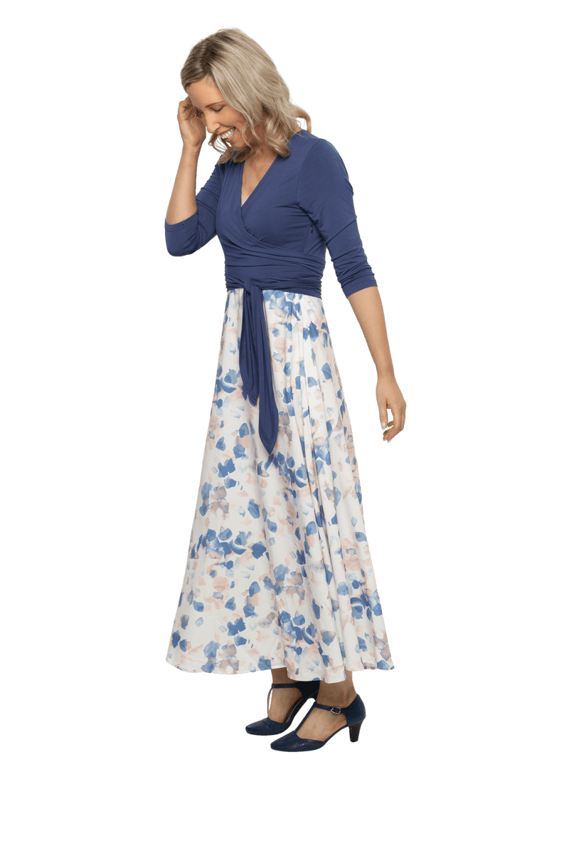 Petite model facing the side wearing maxi dress with blue mid sleeved crossover top attached to white skirt with blue and tan watercolour accents. Mai available in sizes 6-26