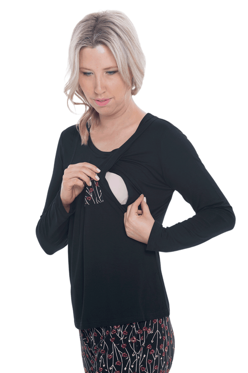 Curvy model facing camera wearing long sleeved pyjamas with pants. Top is black with contrast breast pocket matching pants. Pants are black with small red rose pattern, featuring pockets, and elasticated waist with pull tie. Piper available in sizes 6-26