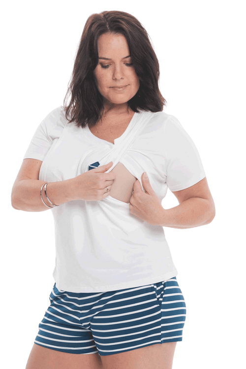 Brunette model facing the camera wearing short sleeved pyjamas with shorts. Top is white with contrast breast pocket matching shorts. Shorts are teal and white stripe, featuring pockets, and elasticated waist with pull tie. Poppy available in sizes 6-18