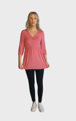 Petite model wearing pink, mid-length sleeved top. Features button up v-neckline and peplum tier under bust. Dylan available in sizes 6-26