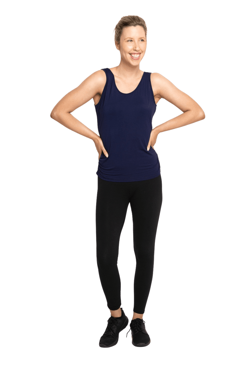 Petite model facing camera wearing navy blue tank top, featuring rounded neckline and side rouching. Adrien available in sizes 6-26