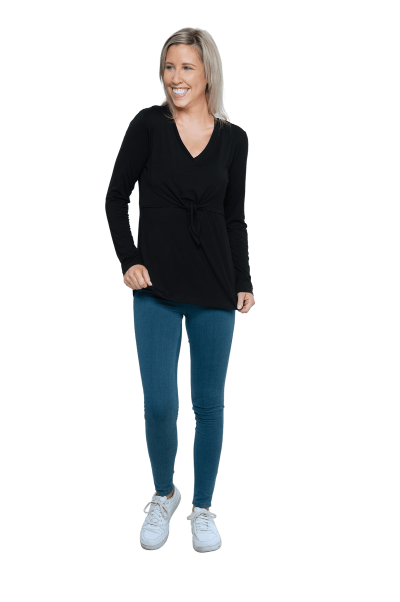 Petite model facing camera wearing black, long sleeved, v-neck top, features small tie front under bust. Billie available in sizes 6-26