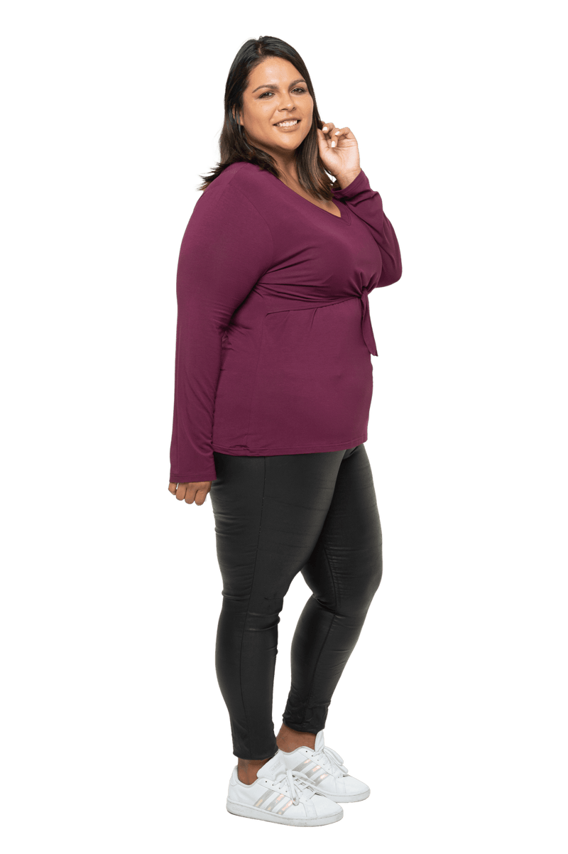 Curvy model facing the side wearing burgundy, long sleeved, v-neck top, features small tie front under bust. Billie available in sizes 6-26