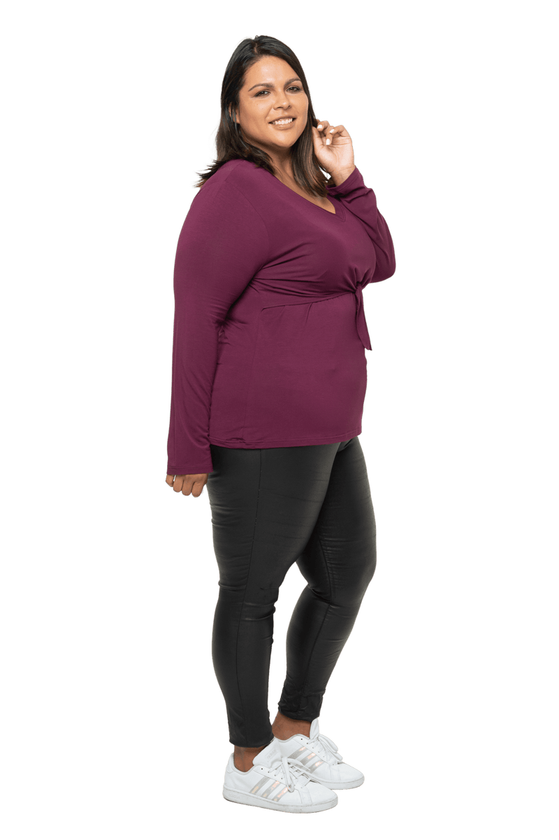 Curvy model facing the side wearing burgundy, long sleeved, v-neck top, features small tie front under bust. Billie available in sizes 6-26