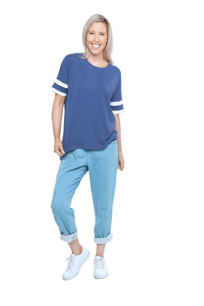 Petite model facing camera wearing navy blue, short sleeved, relaxed fit top, features rounded neckline and two white varsity stripes on the sleeve. Cameron available in sizes 6-26