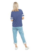 Petite model facing the back wearing navy blue, short sleeved, relaxed fit top, features rounded neckline and two white varsity stripes on the sleeve. Cameron available in sizes 6-26