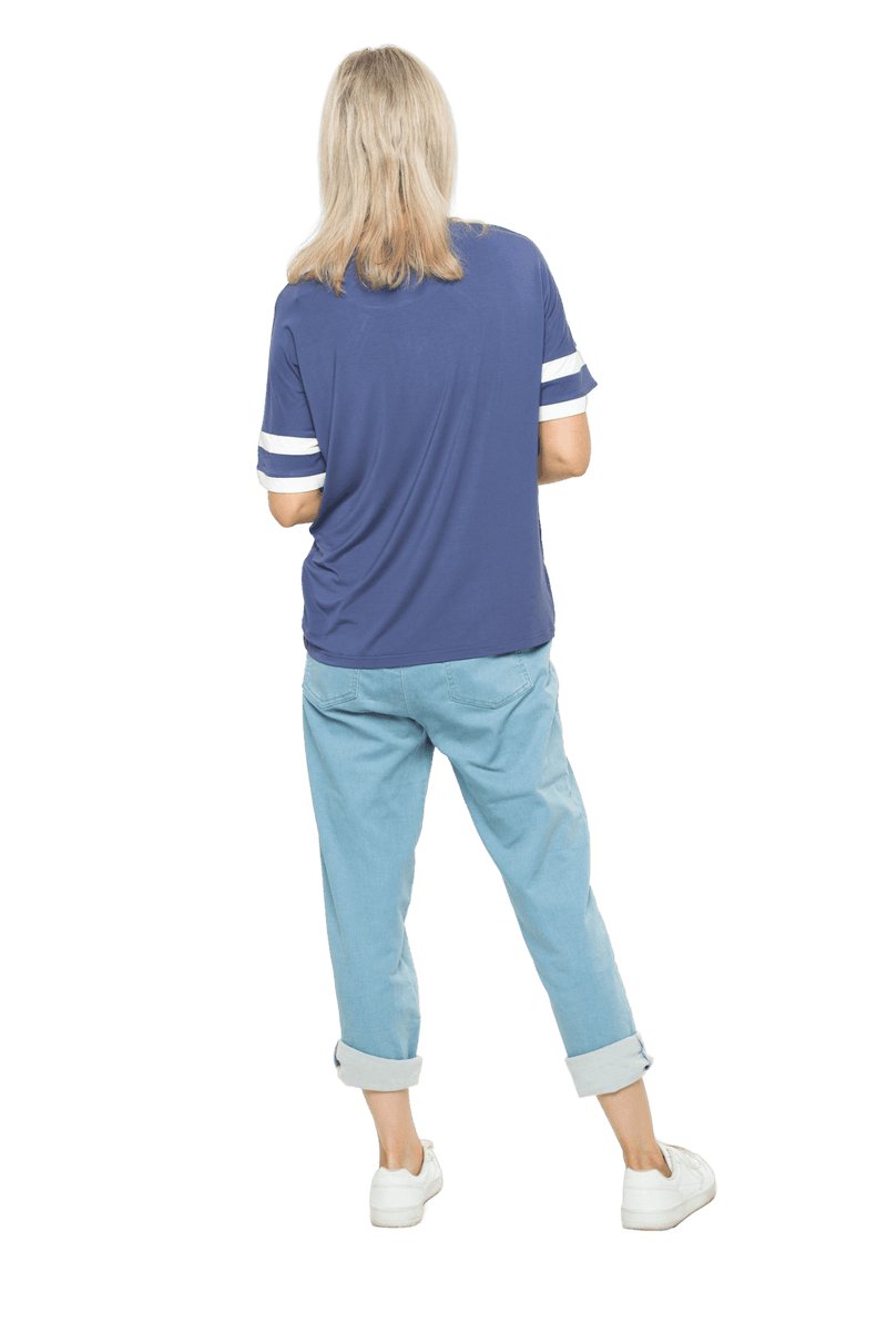 Petite model facing the back wearing navy blue, short sleeved, relaxed fit top, features rounded neckline and two white varsity stripes on the sleeve. Cameron available in sizes 6-26