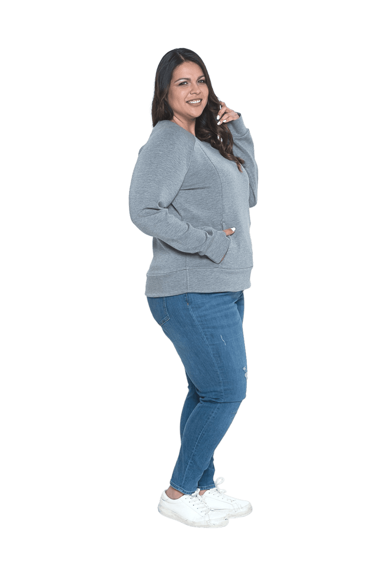 Curvy model facing the side wearing grey crew necked jumper, featuring thick, flat waist band, thumb holes, and pockets. Cassie available in sizes 6-26