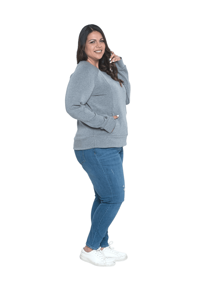 Curvy model facing the side wearing grey crew necked jumper, featuring thick, flat waist band, thumb holes, and pockets. Cassie available in sizes 6-26