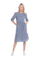 Model facing camera wearing blue gingham, mid-length sleeved midi dress, features rounded neckline, tiered skirt and pockets. Dorothy available in sizes 6-18