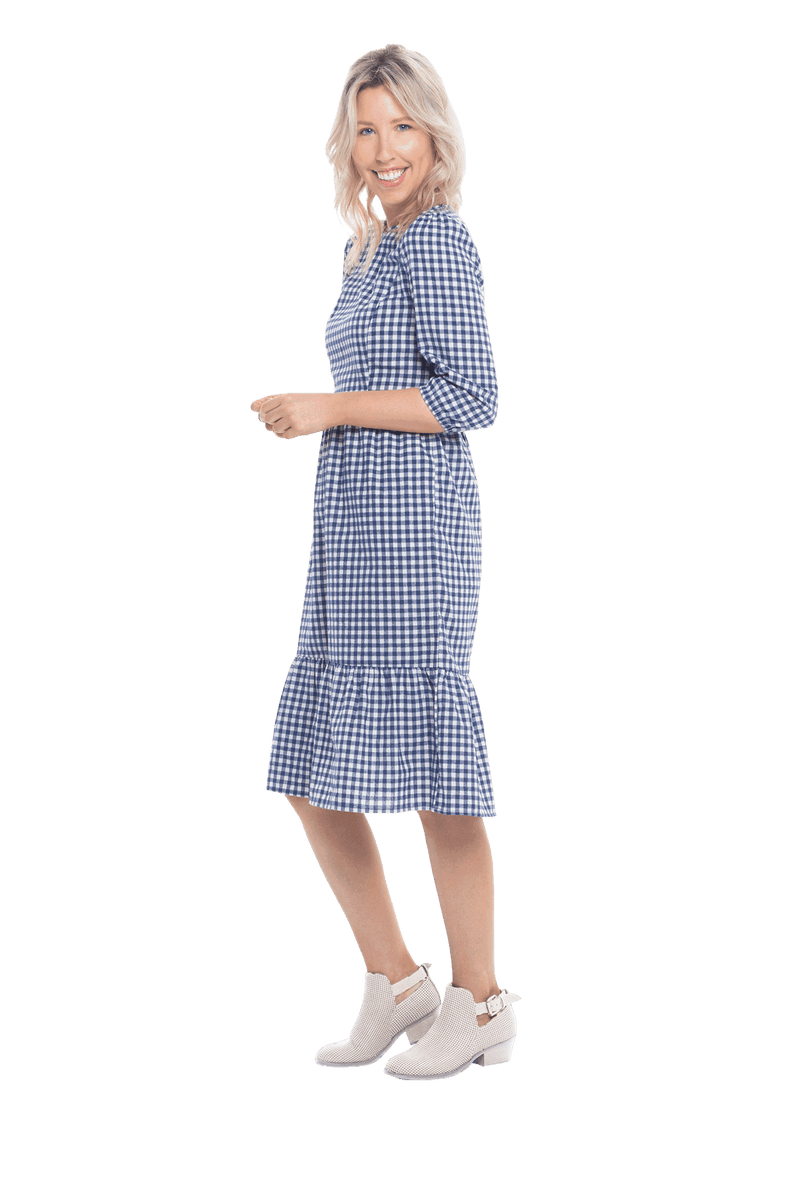 Model facing the side wearing blue gingham, mid-length sleeved midi dress, features rounded neckline, tiered skirt and pockets. Dorothy available in sizes 6-18