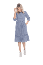 Model facing camera wearing blue gingham, mid-length sleeved midi dress, features rounded neckline, tiered skirt and pockets. Dorothy available in sizes 6-18