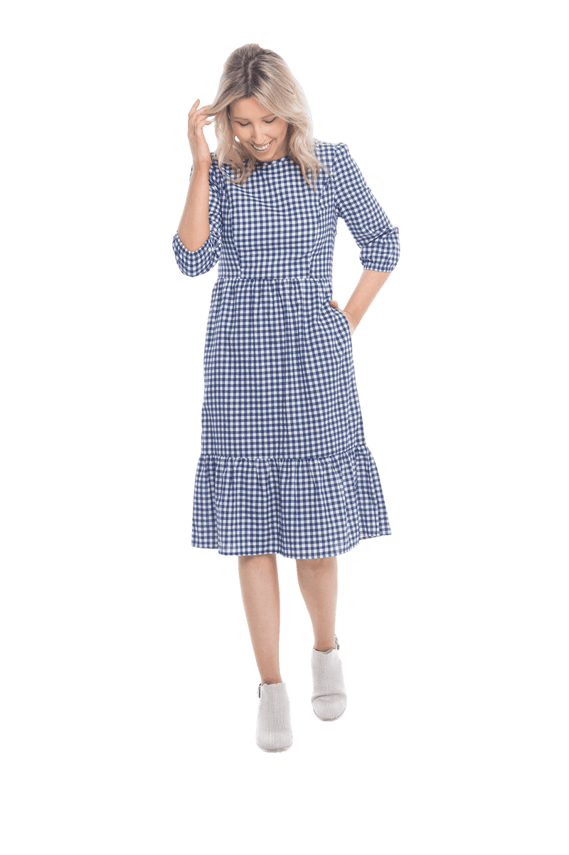 Model facing camera wearing blue gingham, mid-length sleeved midi dress, features rounded neckline, tiered skirt and pockets. Dorothy available in sizes 6-18