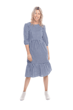 Model facing camera wearing blue gingham, mid-length sleeved midi dress, features rounded neckline, tiered skirt and pockets. Dorothy available in sizes 6-18