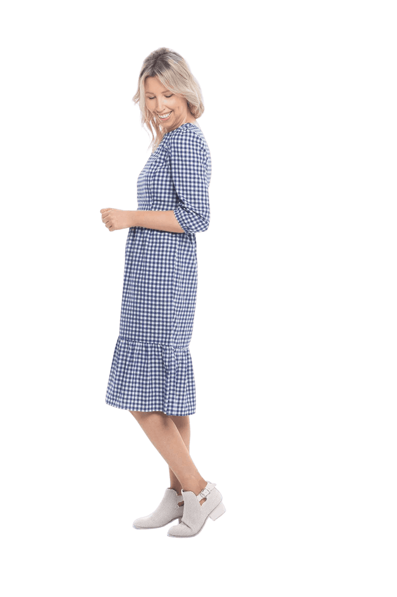 Model facing the side wearing blue gingham, mid-length sleeved midi dress, features rounded neckline, tiered skirt and pockets. Dorothy available in sizes 6-18