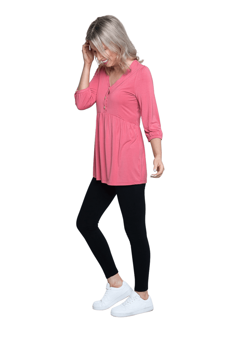 Petite model facing the side wearing pink, mid-length sleeved top. Features button up v-neckline and peplum tier under bust. Dylan available in sizes 6-26