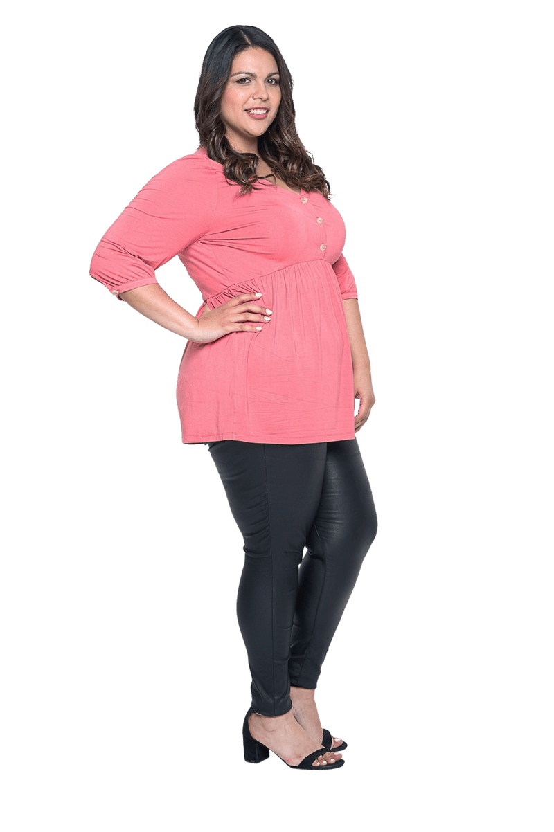 Curvy model facing the side wearing pink, mid-length sleeved top. Features button up v-neckline and peplum tier under bust. Dylan available in sizes 6-26