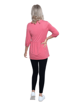 Petite model facing the back wearing pink, mid-length sleeved top. Features button up v-neckline and peplum tier under bust. Dylan available in sizes 6-26