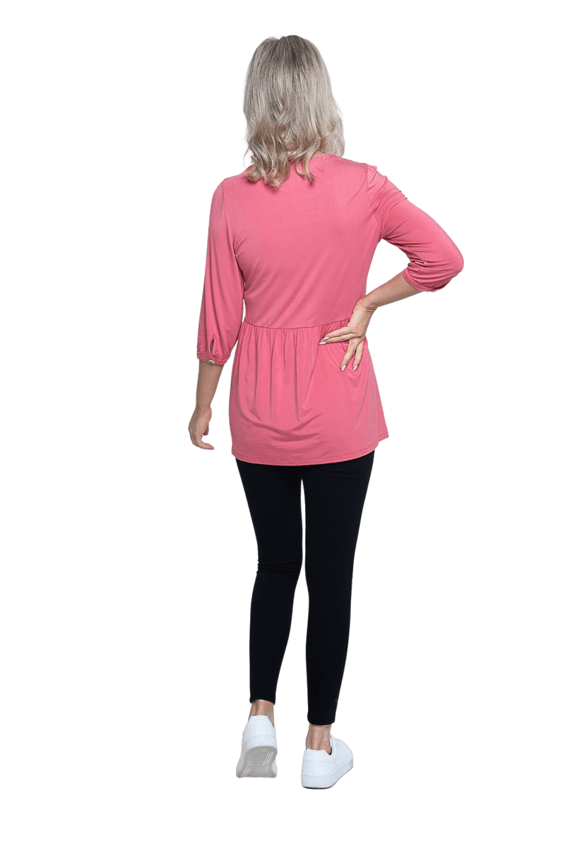 Petite model facing the back wearing pink, mid-length sleeved top. Features button up v-neckline and peplum tier under bust. Dylan available in sizes 6-26