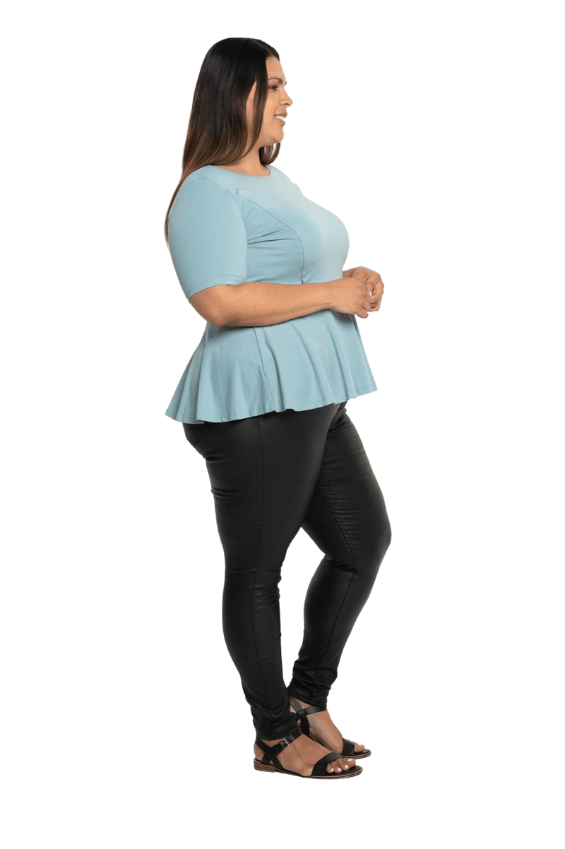 Curvy model facing the side wearing light blue short sleeved top. Featuring rounded neckline and peplum tier under bust. Isla available in sizes 6-26