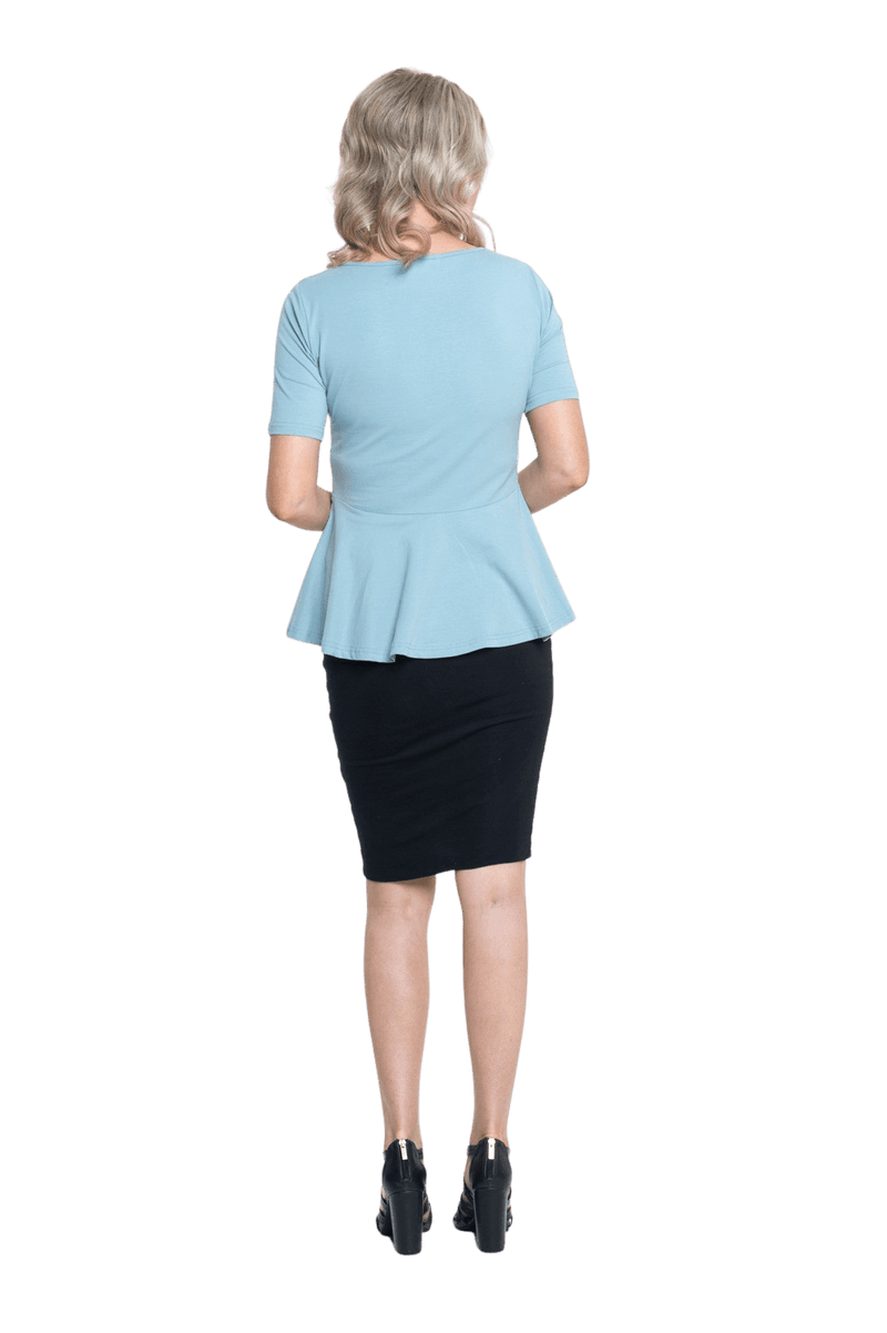 Petite model facing the back wearing light blue short sleeved top. Featuring rounded neckline and peplum tier under bust. Isla available in sizes 6-26