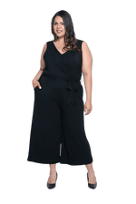 Curvy model facing camera wearing black sleeveless, ankle-length, wide leg jumpsuit, featuring crossover neckline, waist belt and pockets. Jesse available in sizes 6-26