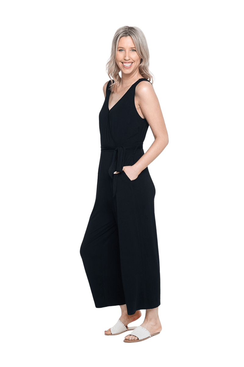 Petite model the side camera wearing black sleeveless, ankle-length jumpsuit, featuring crossover neckline, waist belt and pockets. Jesse available in sizes 6-26