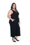 Curvy model facing the side wearing black sleeveless, ankle-length, wide leg jumpsuit, featuring crossover neckline, waist belt and pockets. Jesse available in sizes 6-26