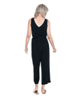 Petite model facing the back wearing black sleeveless, ankle-length jumpsuit, featuring crossover neckline, waist belt and pockets. Jesse available in sizes 6-26