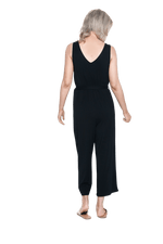 Petite model facing the back wearing black sleeveless, ankle-length jumpsuit, featuring crossover neckline, waist belt and pockets. Jesse available in sizes 6-26