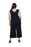 Curvy model facing the back wearing black sleeveless, ankle-length, wide leg jumpsuit, featuring crossover neckline, waist belt and pockets. Jesse available in sizes 6-26