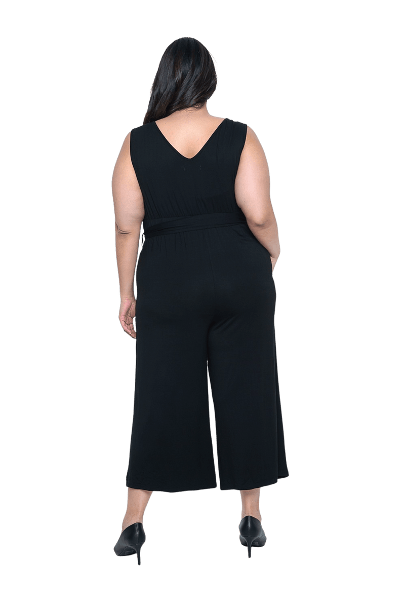Curvy model facing the back wearing black sleeveless, ankle-length, wide leg jumpsuit, featuring crossover neckline, waist belt and pockets. Jesse available in sizes 6-26