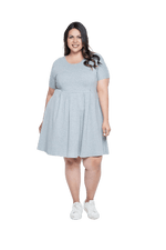 Curvy model facing camera wearing grey with white pin striped, knee length dress, featuring rounded neckline, fitted bodice, pleated A-line skirt and pockets. Kaitlyn available in sizes 6-26