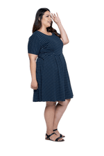 Curvy model facing the side wearing navy with white pin striped, knee length dress, featuring rounded neckline, fitted bodice, pleated A-line skirt and pockets. Kaitlyn available in sizes 6-26