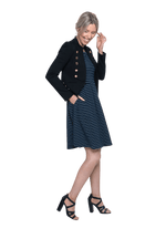 Petite model facing the side wearing navy with white pin striped, knee length dress and black blazer, featuring rounded neckline, fitted bodice, pleated A-line skirt and pockets. Kaitlyn available in sizes 6-26