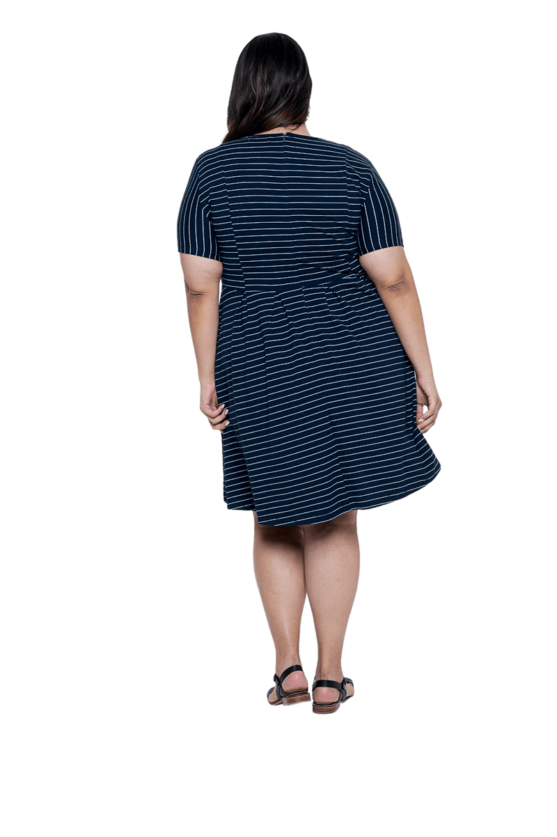 Curvy model facing the back wearing navy with white pin striped, knee length dress, featuring rounded neckline, fitted bodice, pleated A-line skirt and pockets. Kaitlyn available in sizes 6-26