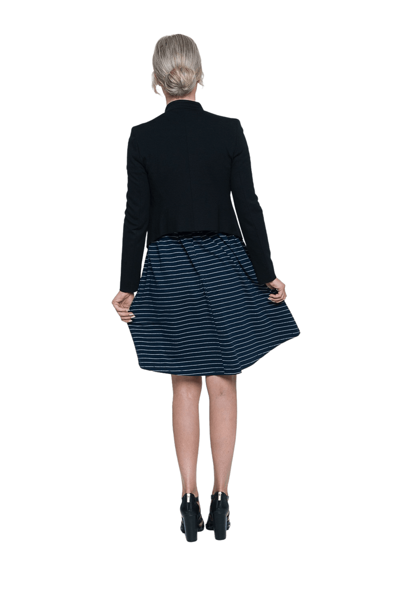 Petite model facing the back wearing navy with white pin striped, knee length dress and black blazer, featuring rounded neckline, fitted bodice, pleated A-line skirt and pockets. Kaitlyn available in sizes 6-26