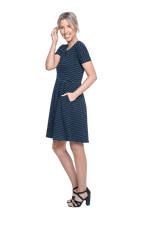 Petite model facing the side wearing navy with white pin striped, knee length dress, featuring rounded neckline, fitted bodice, pleated A-line skirt and pockets. Kaitlyn available in sizes 6-26