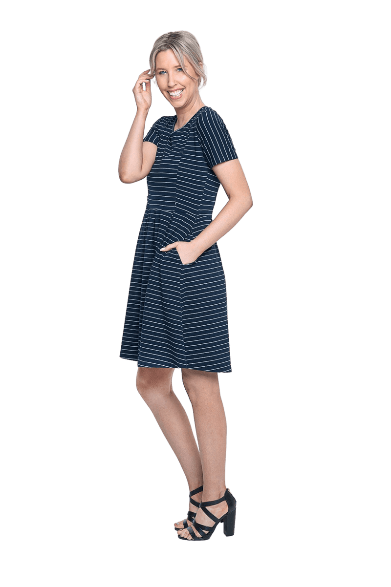 Petite model facing the side wearing navy with white pin striped, knee length dress, featuring rounded neckline, fitted bodice, pleated A-line skirt and pockets. Kaitlyn available in sizes 6-26