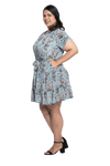 Curvy model facing the side wearing dusty blue with small pink floral, knee-length dress, featuring pockets, a rounded, frilled neckline, and a tiered skirt. Kirsty available in sizes 6-26