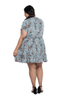 Curvy model facing the back wearing dusty blue with small pink floral, knee-length dress, featuring pockets, a rounded, frilled neckline, and a tiered skirt. Kirsty available in sizes 6-26