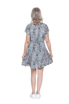 Petite model facing the back wearing dusty blue with small pink floral, knee-length dress, featuring pockets, a rounded, frilled neckline, and a tiered skirt. Kirsty available in sizes 6-26