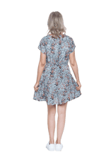 Petite model facing the back wearing dusty blue with small pink floral, knee-length dress, featuring pockets, a rounded, frilled neckline, and a tiered skirt. Kirsty available in sizes 6-26