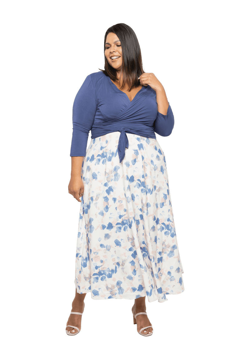 Curvy model facing camera wearing maxi dress with blue mid sleeved crossover top attached to white skirt with blue and tan watercolour accents. Mai available in sizes 6-26