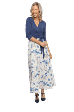 Petite model facing camera wearing maxi dress with blue mid sleeved crossover top attached to white skirt with blue and tan watercolour accents. Mai available in sizes 6-26