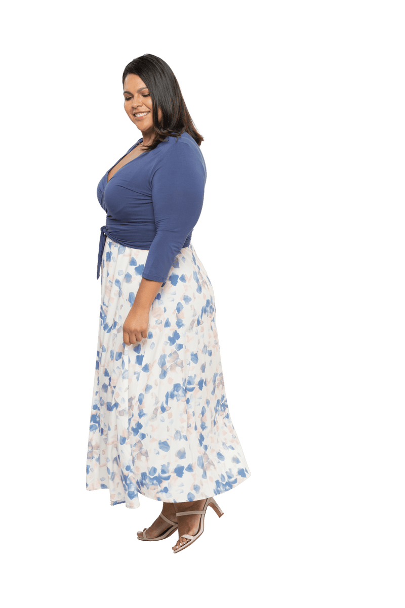 Curvy model facing the side wearing maxi dress with blue mid sleeved crossover top attached to white skirt with blue and tan watercolour accents. Mai available in sizes 6-26