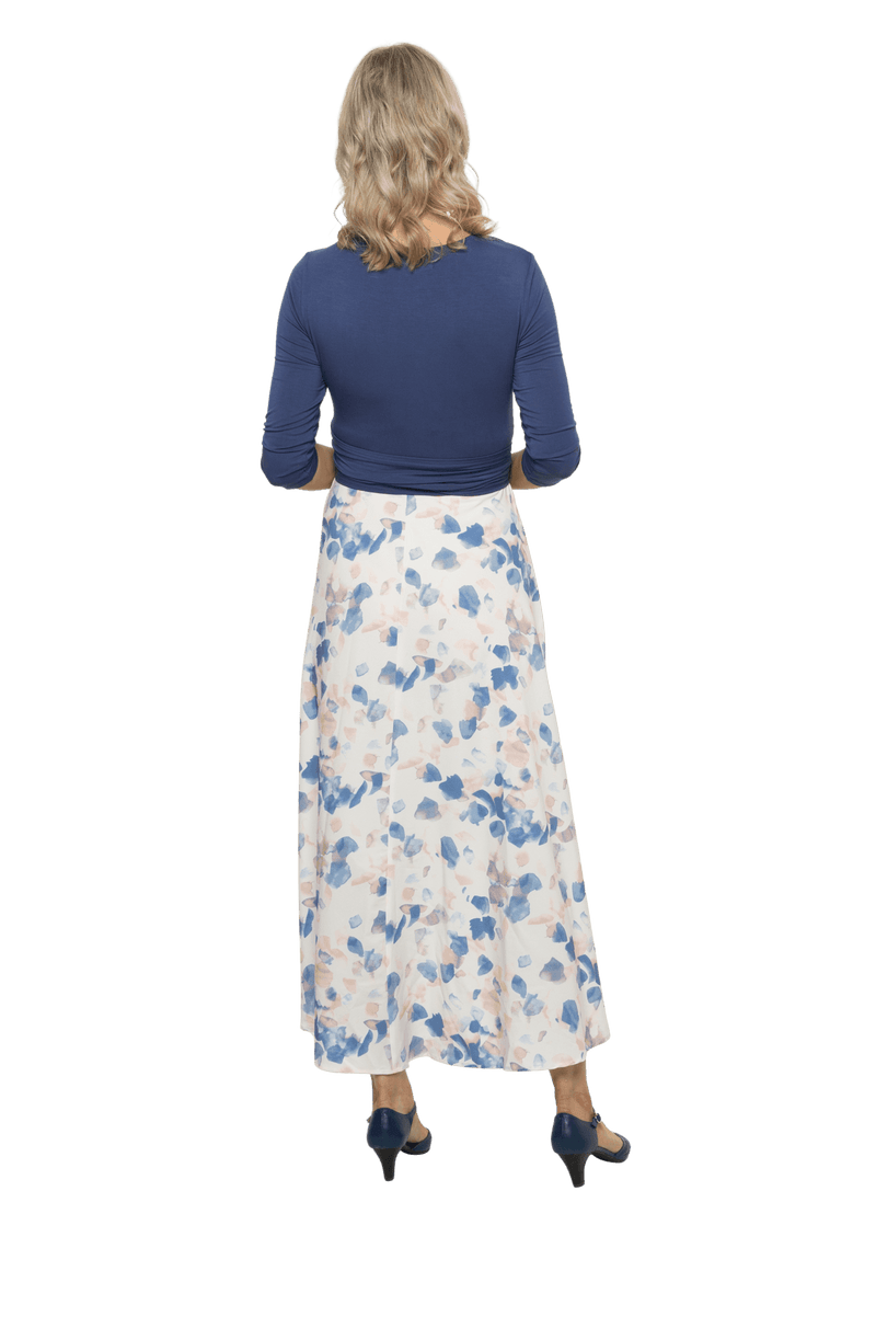 Petite model facing the back wearing maxi dress with blue mid sleeved crossover top attached to white skirt with blue and tan watercolour accents. Mai available in sizes 6-26