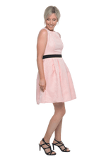 Petite model facing the side wearing pink cocktail dress, featuring a boat neckline, back zip and a feature black sash across the waist. Marie available in sizes 6-18